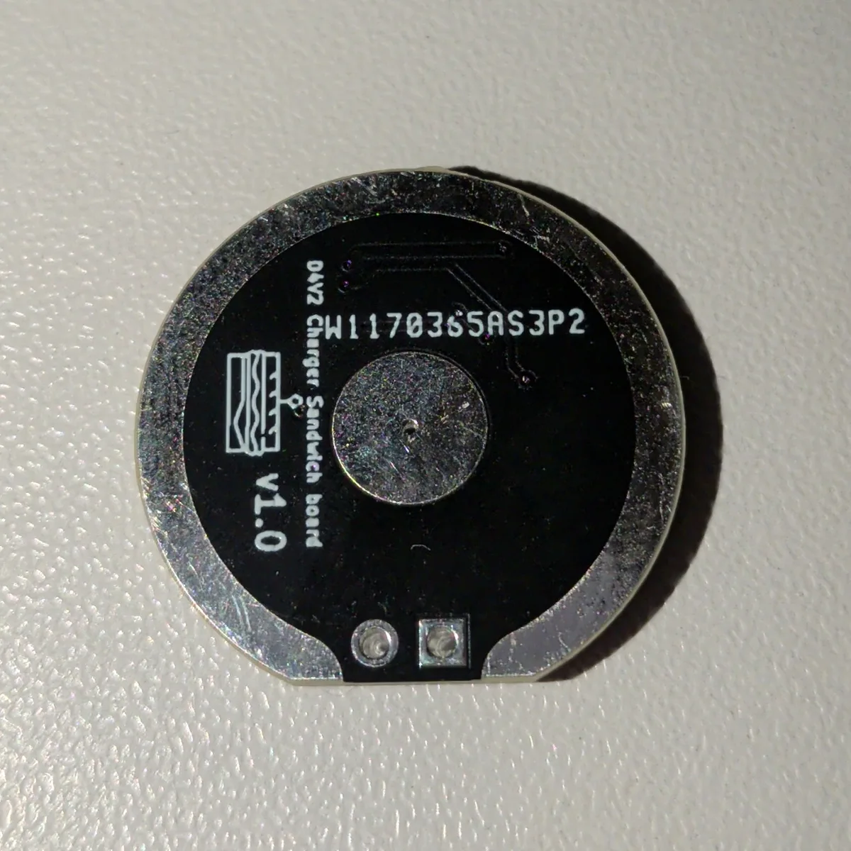 The V1.0 prototype board, back side, with the round spring contact pad, the text D4V2 Charger Sandwich board V1.0 and two pads at the bottom.